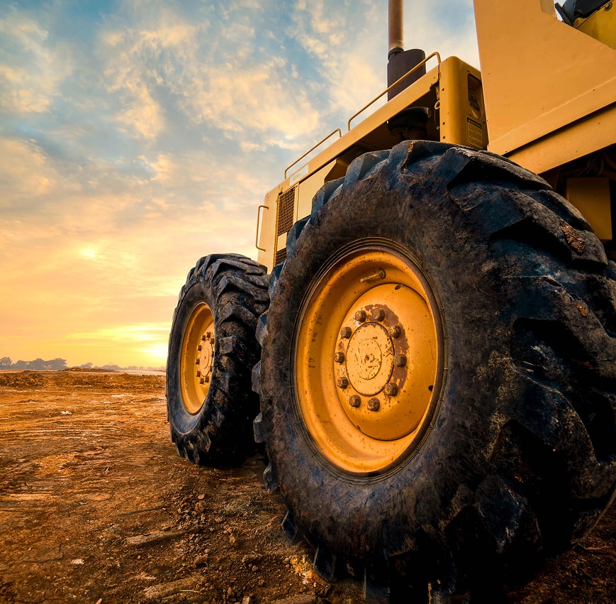 Large yellow construction vehicle with large tires parked on dirt field at sunset.