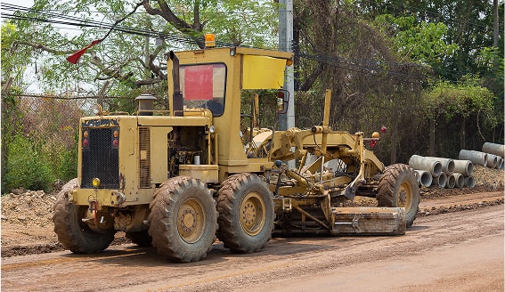 Yellow road grader on a dirt road.